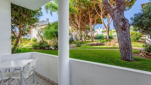 Ein Balkon mit weißem Tisch und Stühlen, der auf einen gepflegten Garten mit verschiedenen Bäumen und einer Rasenfläche blickt.