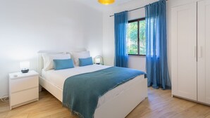 Ein Schlafzimmer mit Bett, Nachttischen, einem Kleiderschrank und einem Fenster mit Vorhängen.