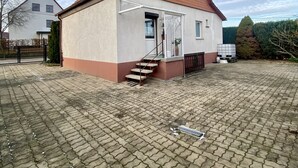 A single-story building with a sloped roof, a set of stairs leading to a door, and a paved courtyard.