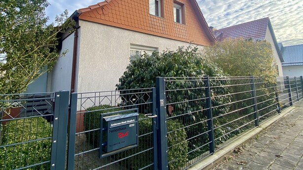 A house with a red roof, a gated entrance, and a mailbox.