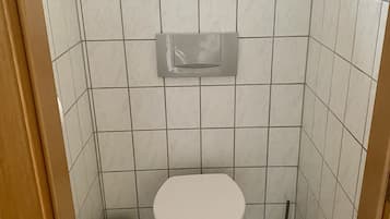Une petite salle de bain carrelée, équipée de toilettes, d’une poubelle et d’un sèche-mains.