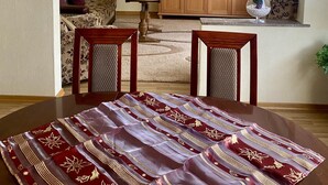 A living room with a sofa, a TV, a wooden cabinet, and a dining table with a table runner.