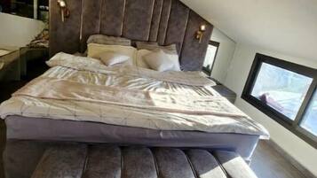 Un dormitorio moderno con una cama grande, un banco empotrado y un ventanal que deja entrar luz natural.