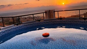Une piscine sur le toit offrant une vue sur le coucher de soleil, un objet orange flottant et un paysage urbain en arrière-plan.