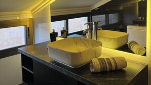 Une cuisine moderne dotée d’un grand îlot central, de plans de travail noirs et d’un évier en marbre blanc.