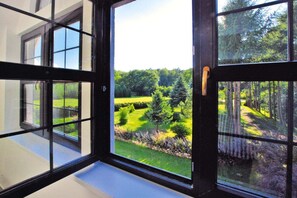 A view through a window with a black frame, revealing a green landscape with trees and a clear sky.