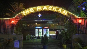 En restaurangentrén med en neonskylt som visar texten ”THE MACHAN” och försäljningsautomater för Pepsi och Coca-Cola.