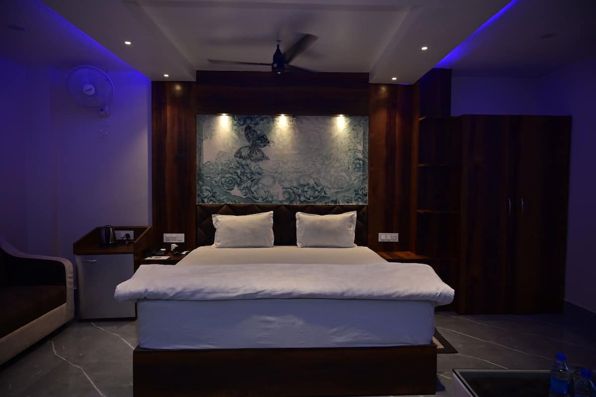 A modern hotel room with a large bed, a nightstand, a desk, and a wardrobe.