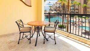 Un balcon avec une table ronde et quatre chaises, donnant sur un espace piscine agrémenté de palmiers et avec un bâtiment en arrière-plan.