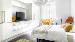 A modern bedroom with a bed, a television on a stand, a chair, and a desk with a lamp. - Spacious apt on Tranquil Courtyard (Helsinki)