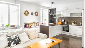 A modern kitchen with white cabinetry, a central island, and a dining area with a wooden table. - Spacious apt on Tranquil Courtyard (Helsinki)
