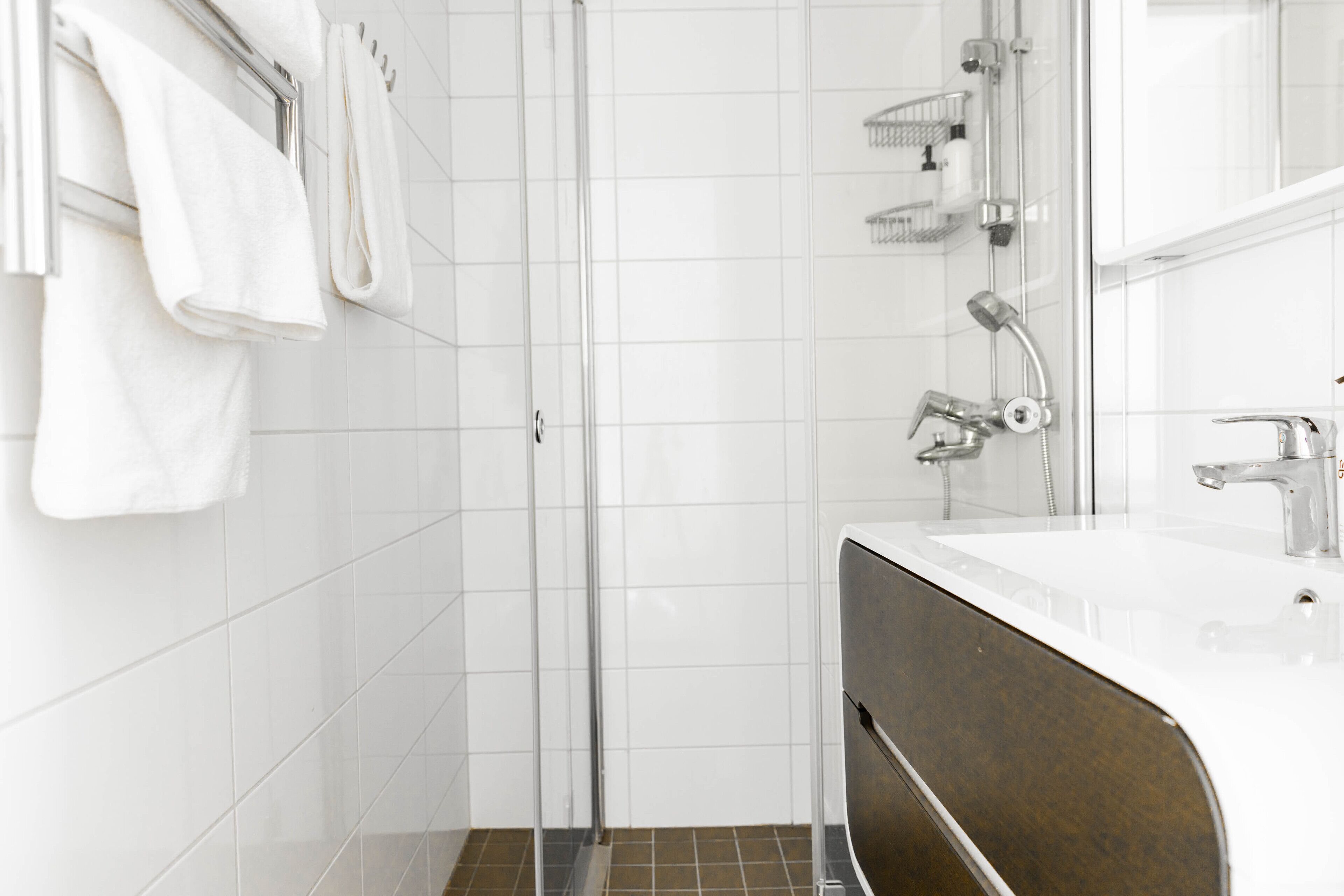 Un bagno moderno con box doccia in vetro, un lavandino bianco su mobile marrone e asciugamani bianchi su un portascopevoli.