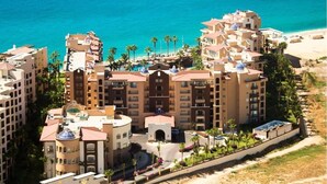 A multi-story hotel with a central courtyard, surrounded by palm trees and a beach. - Christmas in Cabo Dec 21-29, 2024 (Cabo San Lucas)