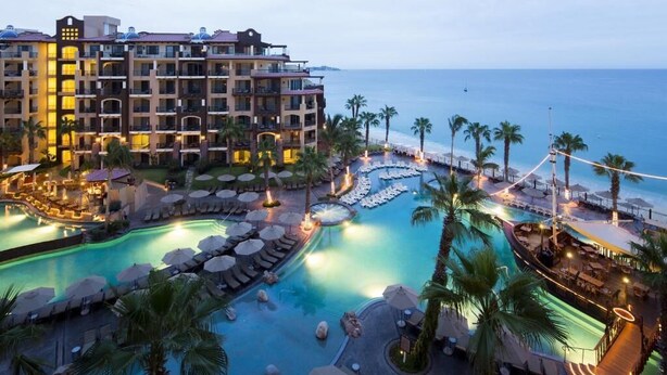 A hotel with multiple swimming pools, palm trees, and a view of the sea. - Christmas in Cabo Dec 21-29, 2024 (Cabo San Lucas)
