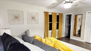 A modern living room with a sofa, a ceiling fan, and two abstract wall art pieces. - The Blissful Hideaway w/ large backyard, jacuzzi and two connecting decks (Villa Rica)