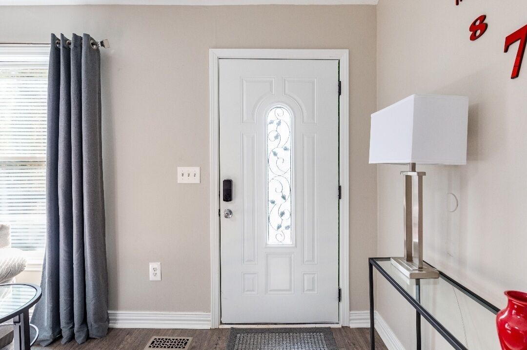 A white door with a glass panel, a grey curtain, a white lamp on a glass table, and a red vase.