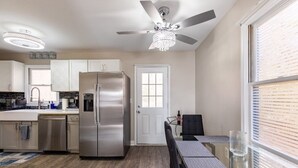 A modern kitchen with stainless steel appliances, a dining area with a glass table, and a ceiling fan. - The Blissful Hideaway w/ large backyard, jacuzzi and two connecting decks (Villa Rica)
