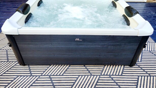 A spa hot tub with a control panel, set against a wooden wall and a patterned floor. - The Blissful Hideaway w/ large backyard, jacuzzi and two connecting decks (Villa Rica)