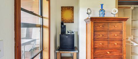 Ein gemütlicher Raum mit einer Kaffeemaschine auf einem kleinen Tisch, einem Holzschrank und einem Fenster mit Blick auf Gartenmöbel.