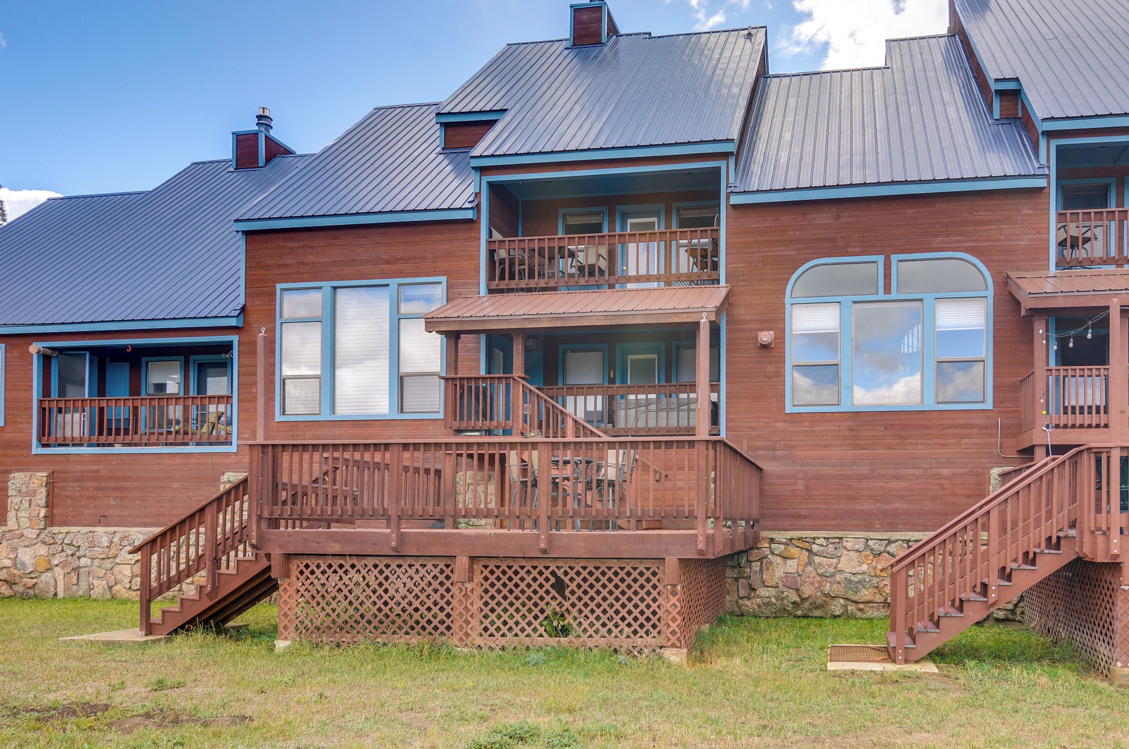 A two-story wooden house with a balcony, stone foundation, and a metal roof.