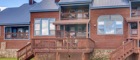 A two-story wooden house with a balcony, stone foundation, and a metal roof.