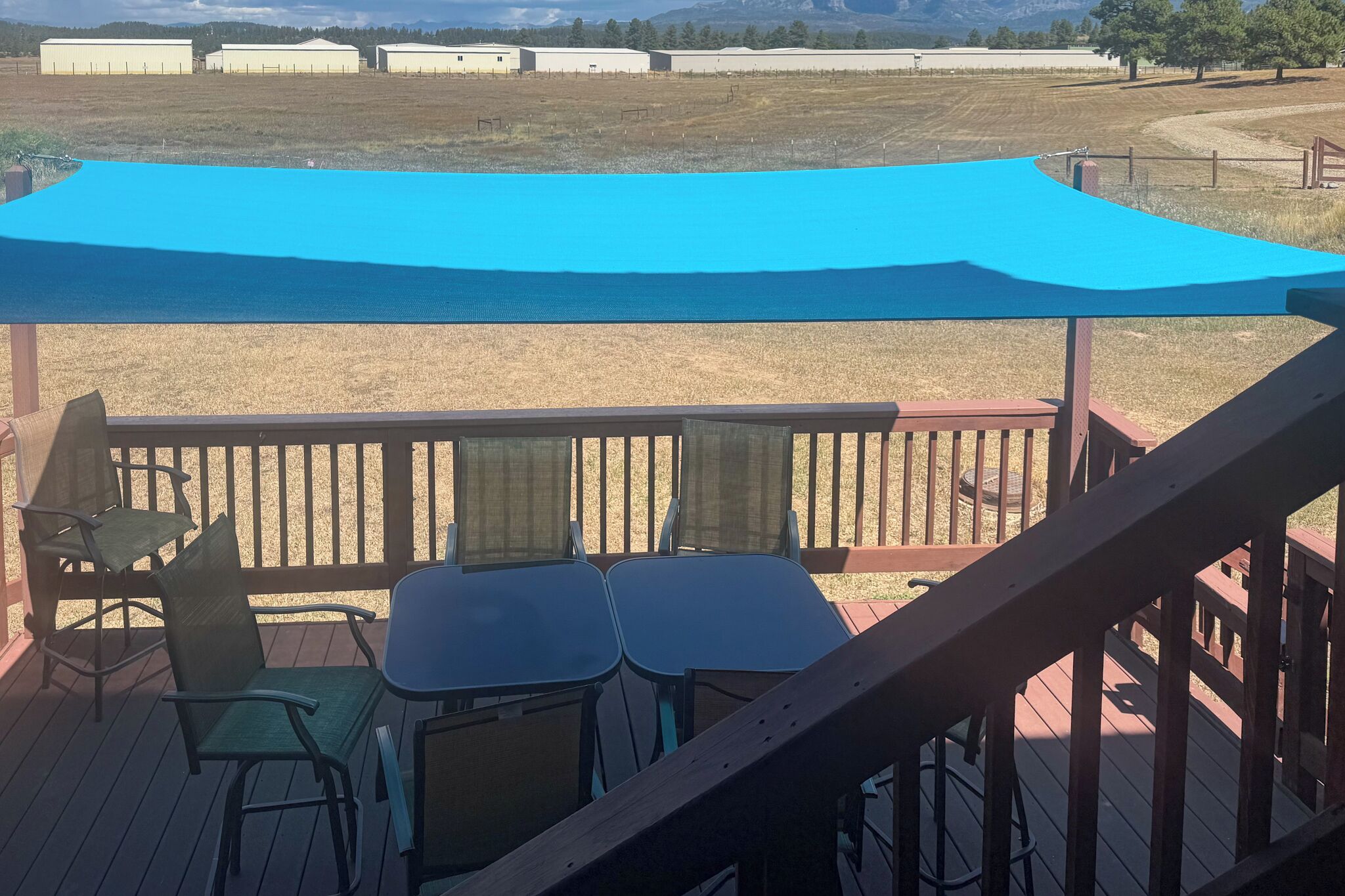 Een overdekt terras met een tafel en stoelen, met uitzicht op een veld met gebouwen in de verte.