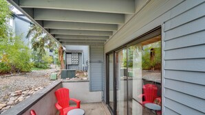 A covered patio area with red chairs and a small table, a sliding glass door leading to a garden, and a metal utility box. - Steamboat Springs Condo Near Ski Resort & Village! (Steamboat Springs)