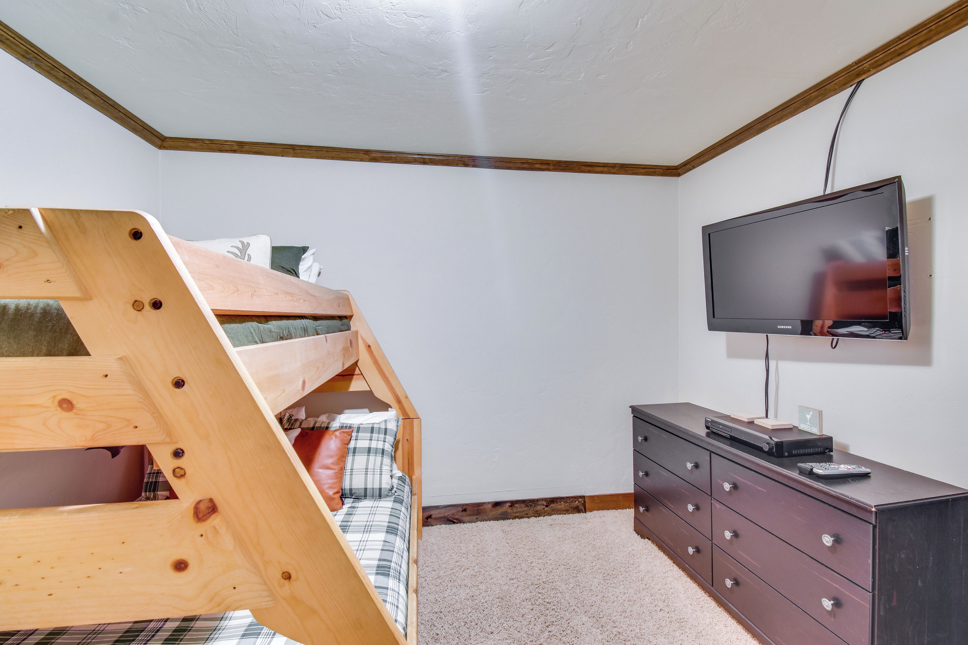 A bedroom with a bunk bed, a dresser, and a television on the wall.