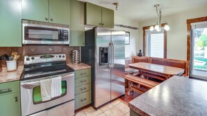 A kitchen with green cabinets, a stainless steel refrigerator, a microwave, and an oven. There is a wooden dining table and bench. - Steamboat Springs Condo Near Ski Resort & Village! (Steamboat Springs)