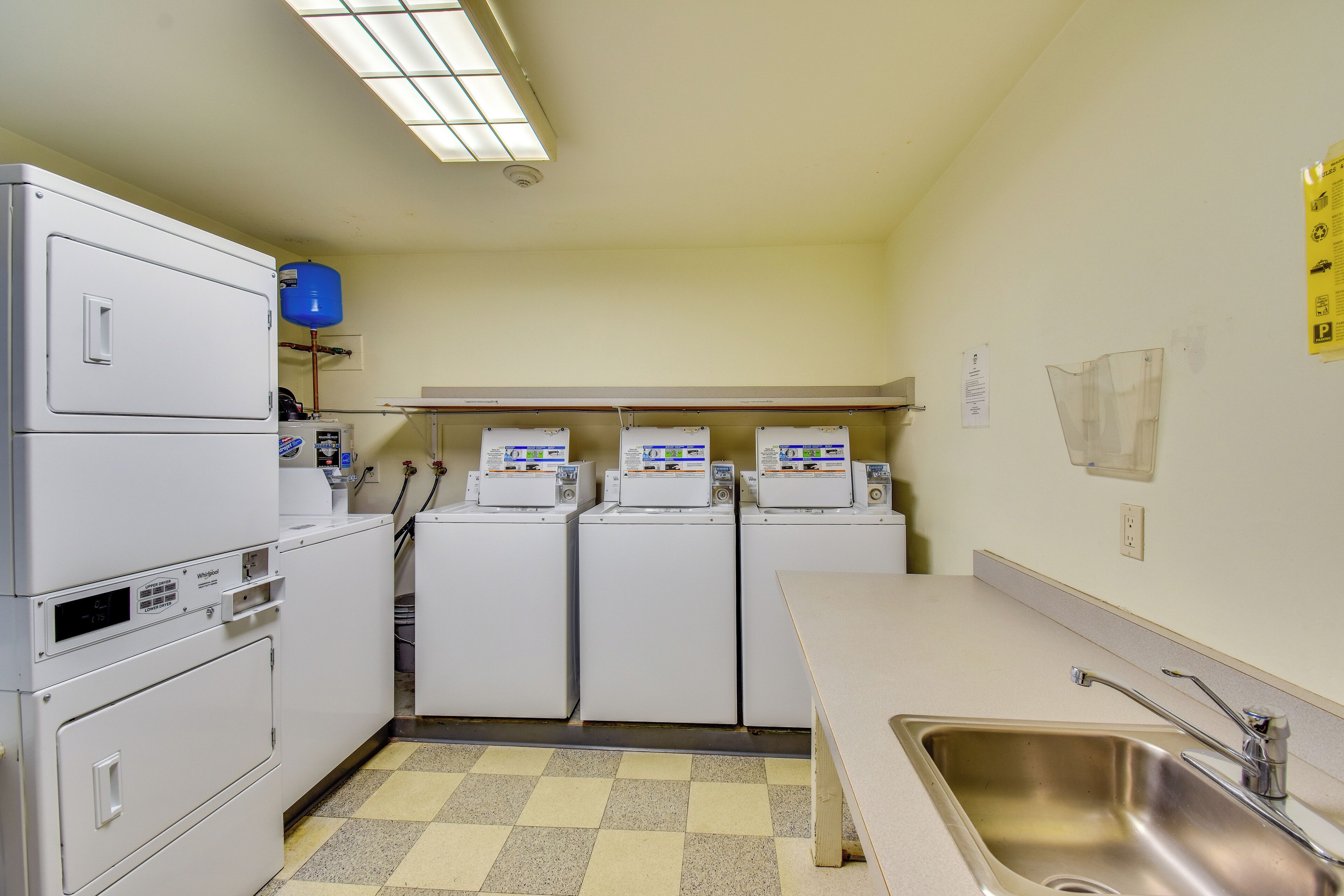 A kitchen with a stainless steel sink, a water heater, and a checkered floor.