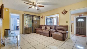 A living room with a brown leather sofa, a glass coffee table, a ceiling fan, and a tiled floor. - 4 Mi to Beach: Hollywood Home w/ Patios! (Hollywood)