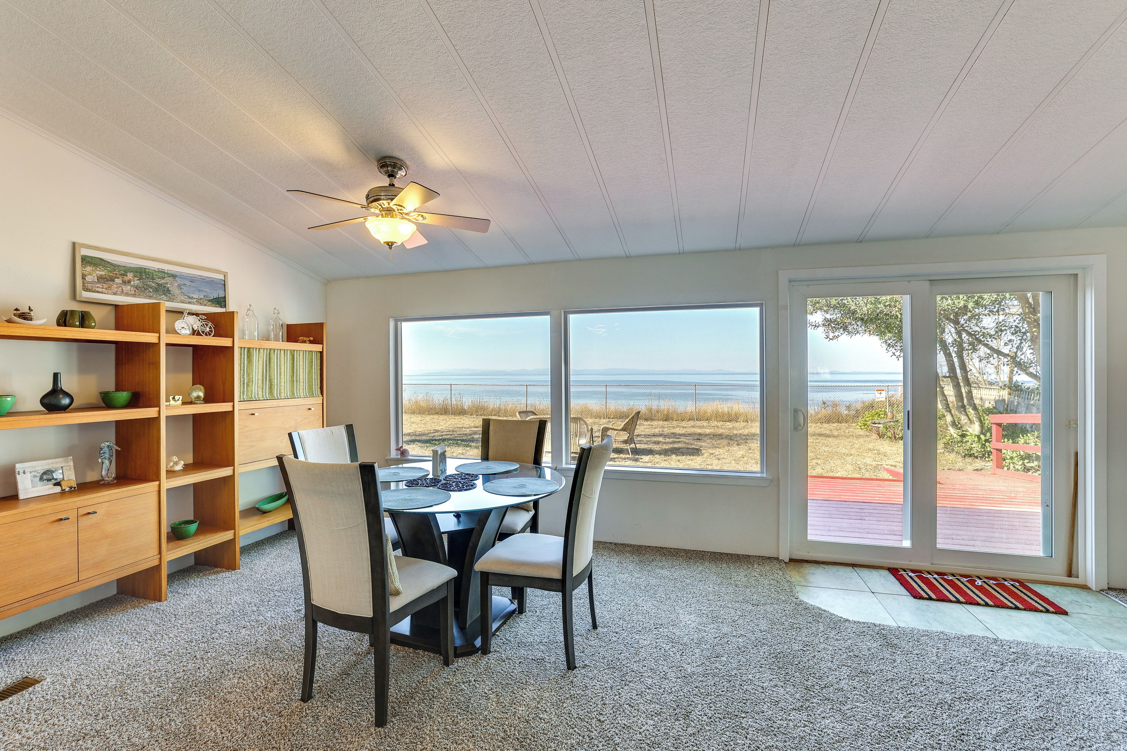 A dining area with a table and chairs, a ceiling fan, and a view of the beach through large windows.