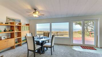 A dining area with a table and chairs, a ceiling fan, and a view of the beach through large windows.