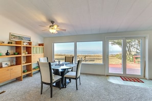 A dining area with a table and chairs, a ceiling fan, and a view of the beach through large windows. - Oceanfront Port Angeles Home w/ Yard & Views! (Port Angeles)