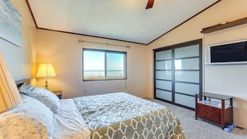 A bedroom with a bed, a window, a ceiling fan, and a TV mounted on the wall.