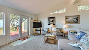 A spacious living room with a large TV, comfortable seating, and artwork on the walls.