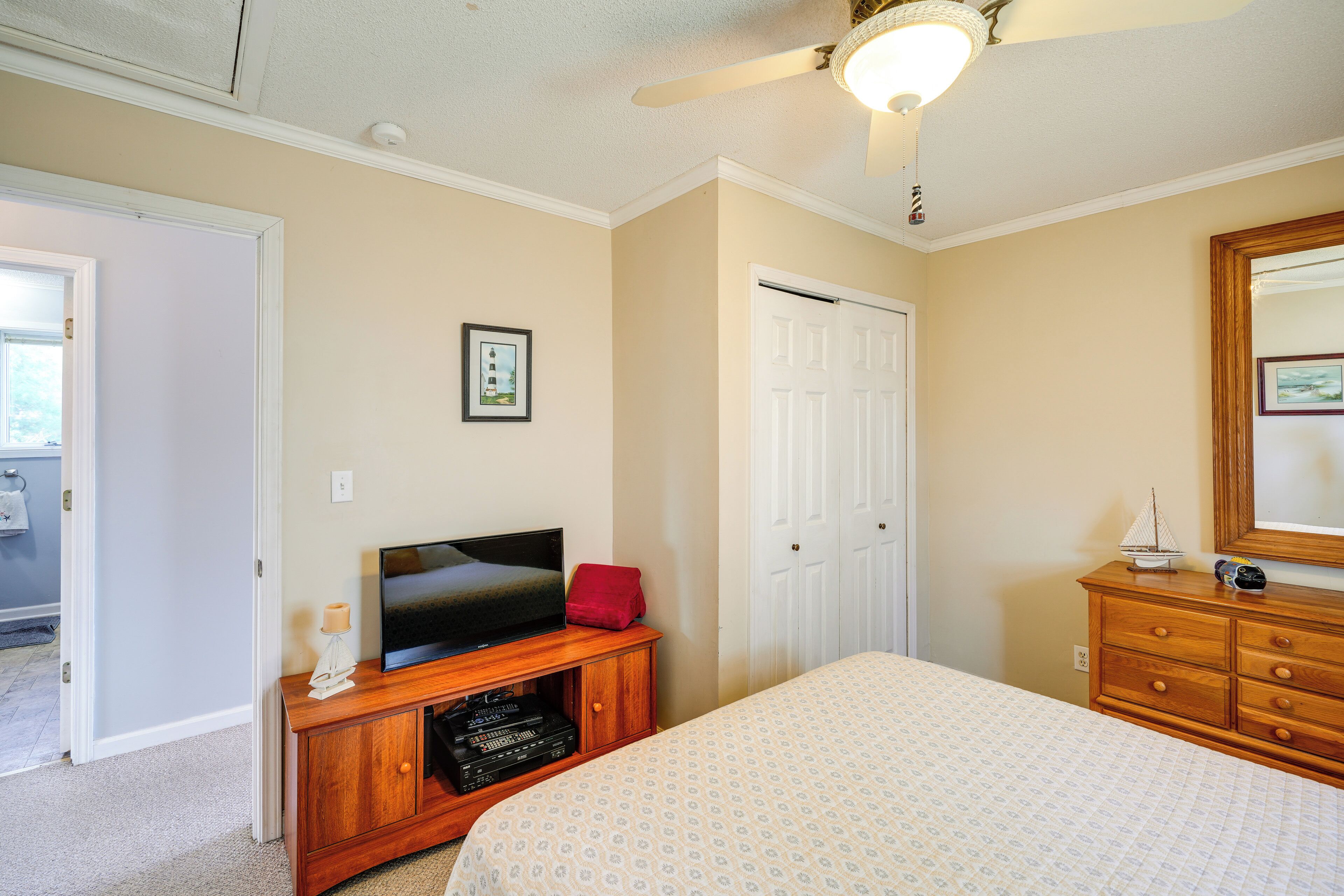 A bedroom with a bed, a TV on a wooden cabinet, a door, and a dresser with a mirror.