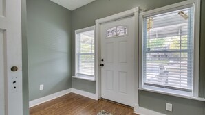 A hallway with a wooden floor, a patterned rug, a white door with a decorative glass panel, and a window with blinds.