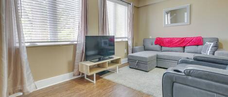 A living room with a gray sectional sofa, a flat-screen TV on a wooden stand, and a red throw blanket.
