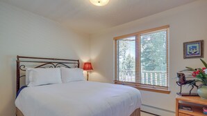 Een slaapkamer met een bed, een nachtkastje, een raam met jaloezieën, een lamp en een foto aan de muur.