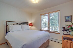 Une chambre à coucher avec un lit, une table de chevet, une fenêtre avec des stores, une lampe et un tableau au mur.