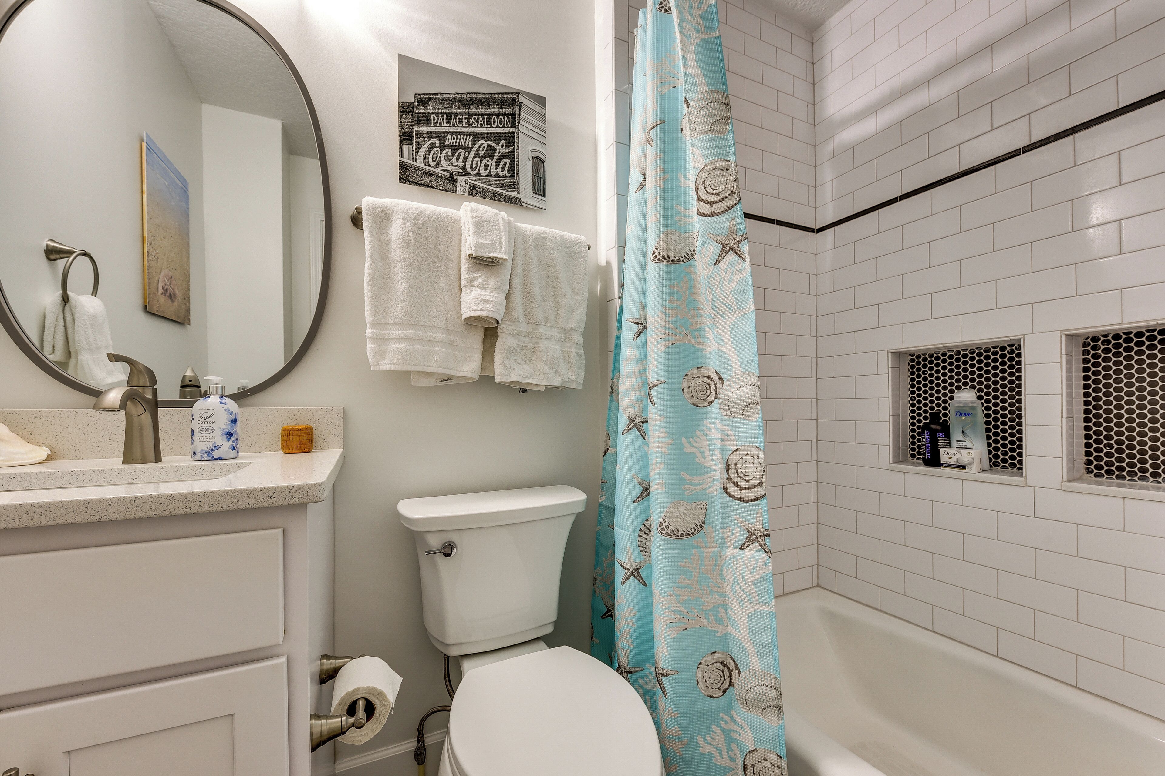 A bathroom with a toilet, sink, and mirror. There are towels hanging on the wall and a shower curtain with a sea shell pattern.