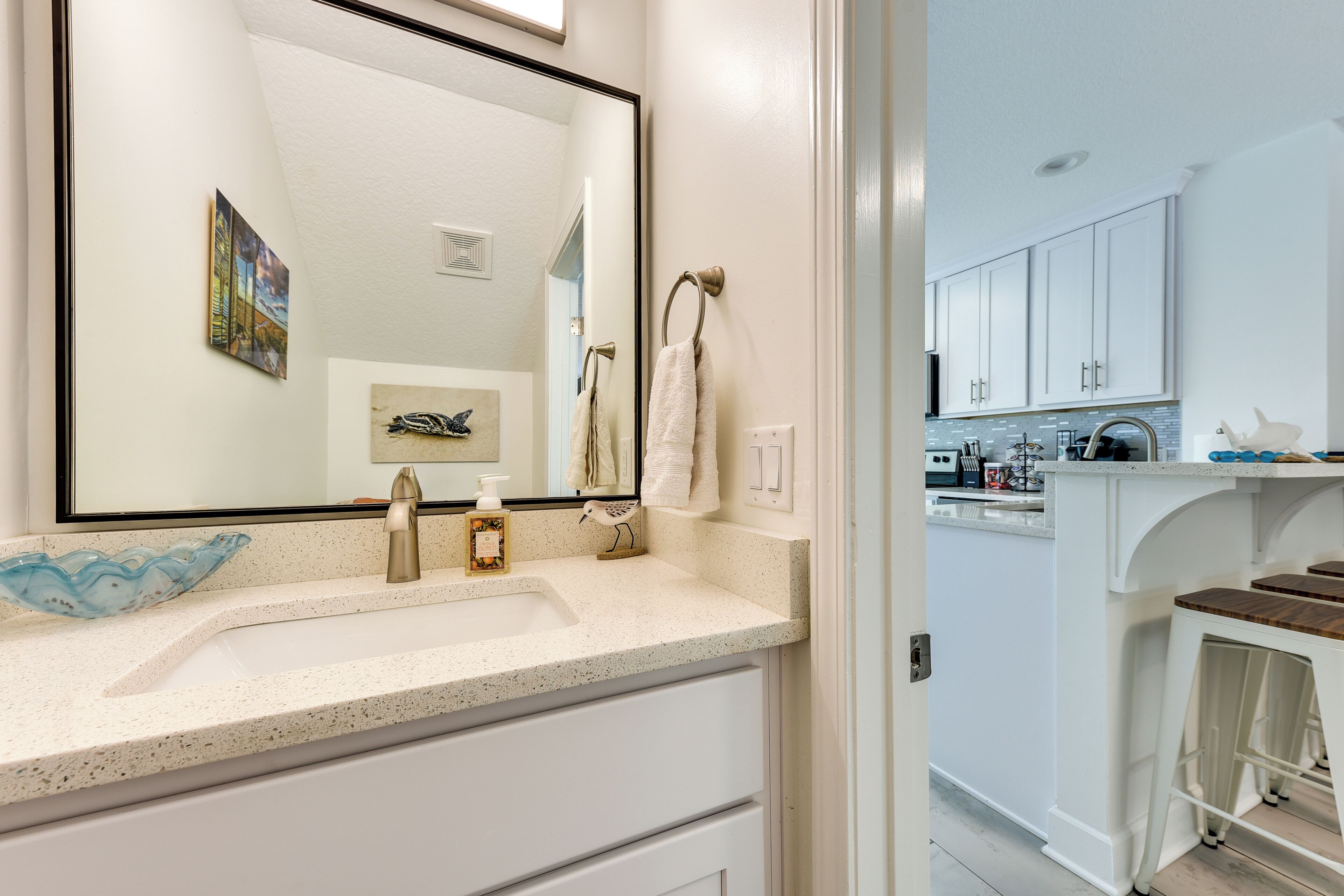 A modern bathroom with a large mirror, a sink with a soap dispenser, and a towel rack.