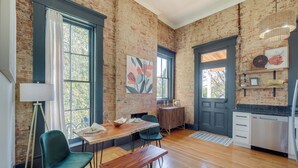 A modern kitchen with wooden flooring, a dining area with a table and chairs, and a brick wall. - Chic & Historic Apartment ~ 6 Mi to Louisville! (New Albany)