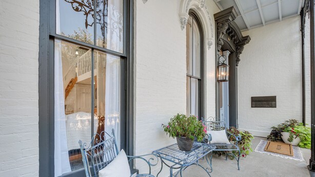 A covered outdoor seating area with metal chairs and tables, potted plants, and a white brick wall. - Chic & Historic Apartment ~ 6 Mi to Louisville! (New Albany)