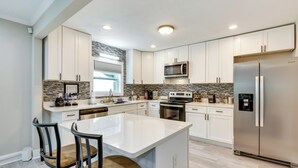 A modern kitchen with white cabinetry, a central island, stainless steel appliances, and a tiled backsplash. - Updated Atlanta Home ~ 5 Mi to Downtown! (Atlanta)