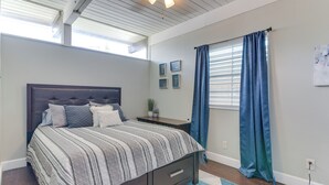 Quarto com uma cama grande, mesa de cabeceira, janela com cortinas azuis e ventilador de teto.