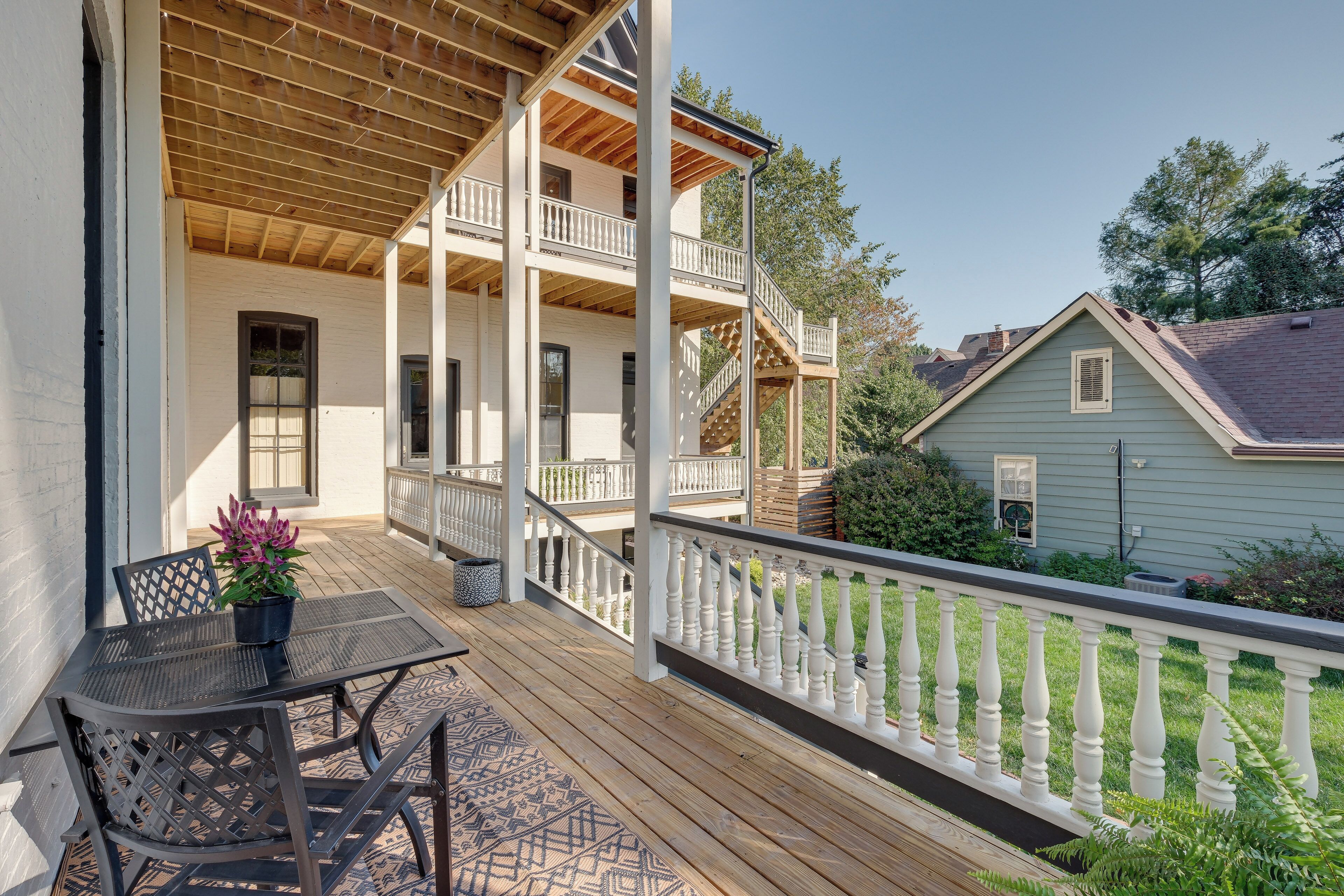 A wooden deck with a white railing, a table with chairs, and a potted plant.