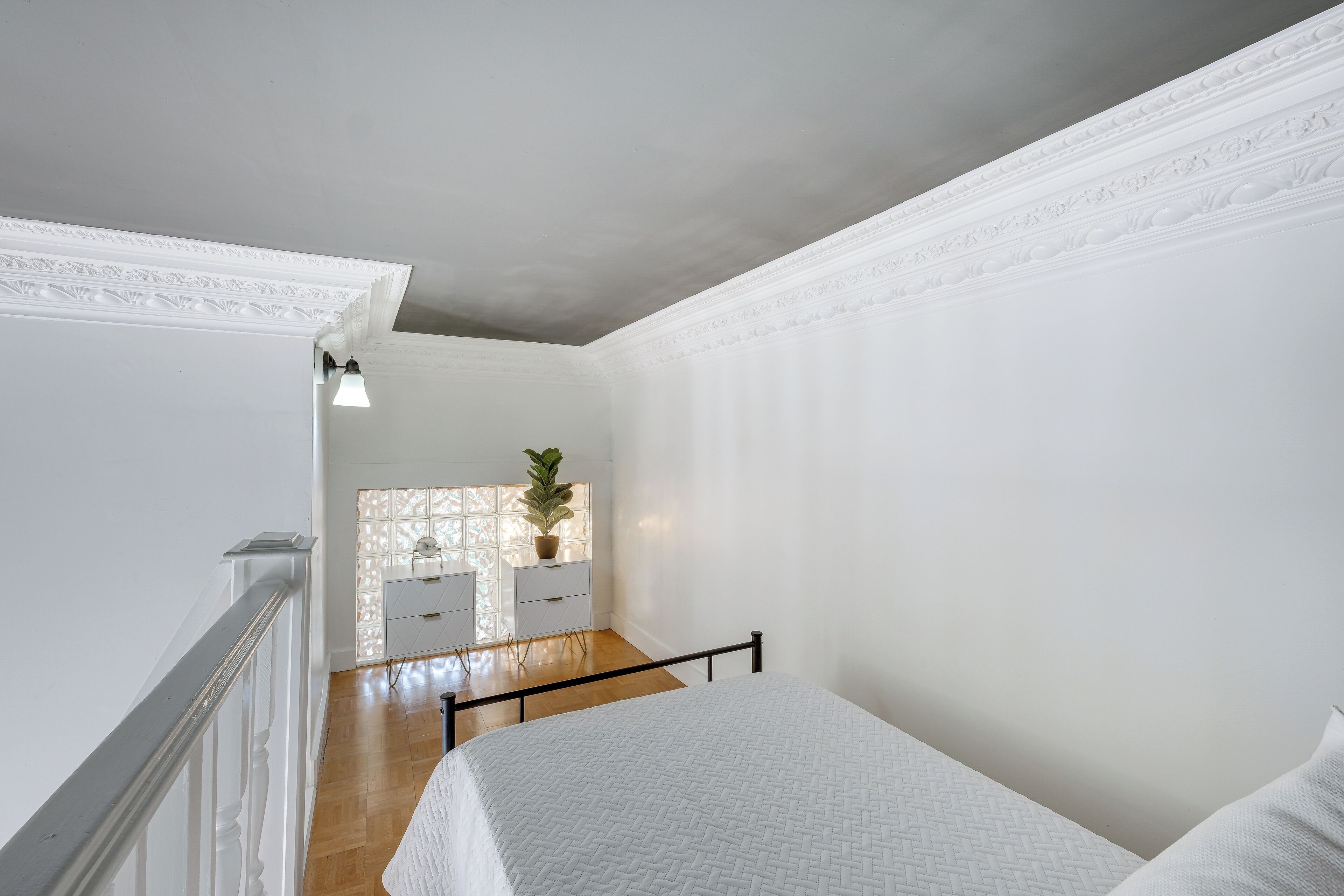 A bedroom with a bed, a dresser, a potted plant, and a window with a view of the outside.