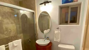 Un baño con ducha de vidrio, un espejo redondo, un lavamanos y un inodoro.